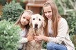 Two cute girls holding labrador dog in park. Looking at camera. Childhood. Friendship.